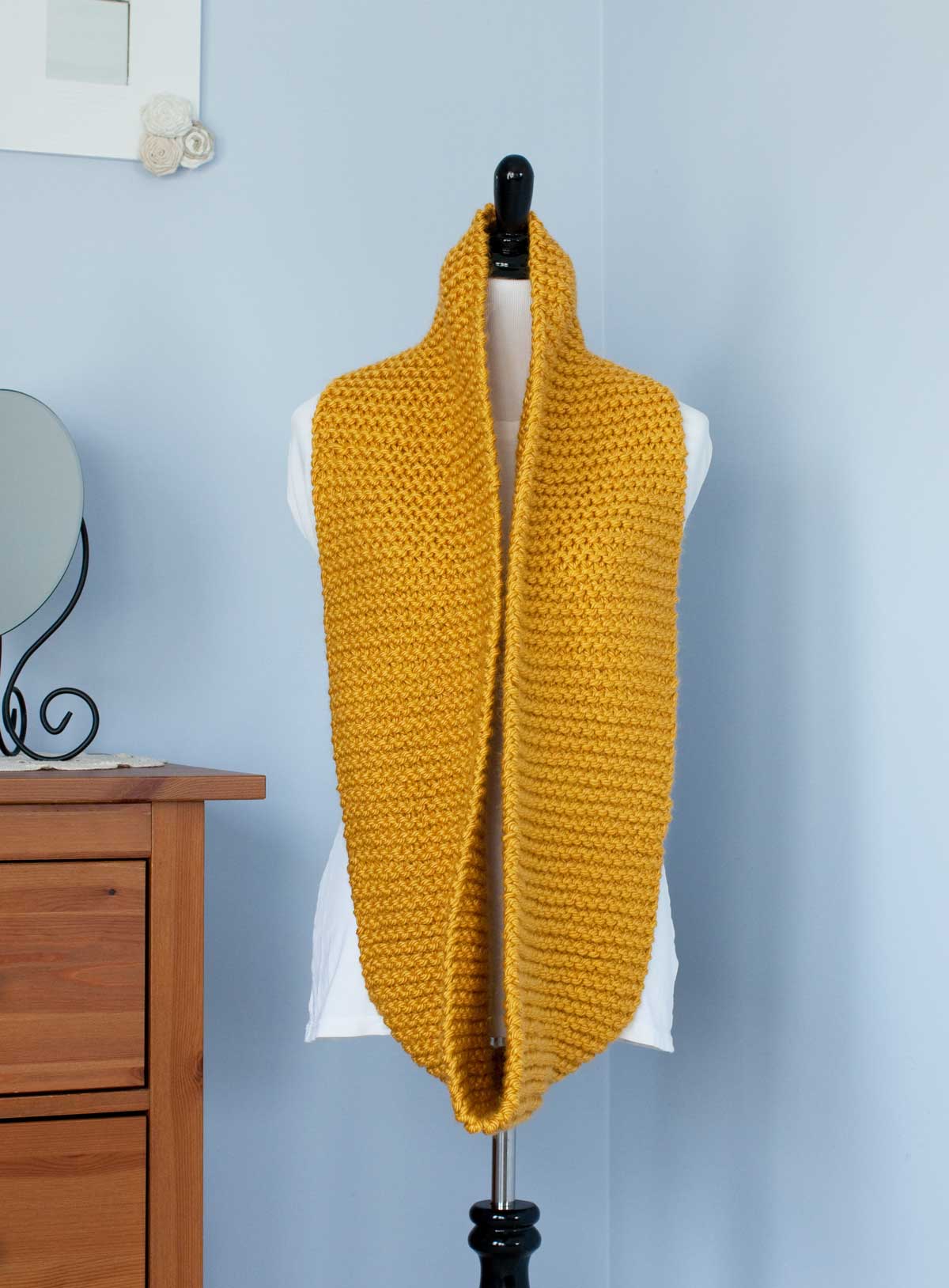 Mustard yellow scarf shown at full width hung around the neck of a dress-makers dummy.