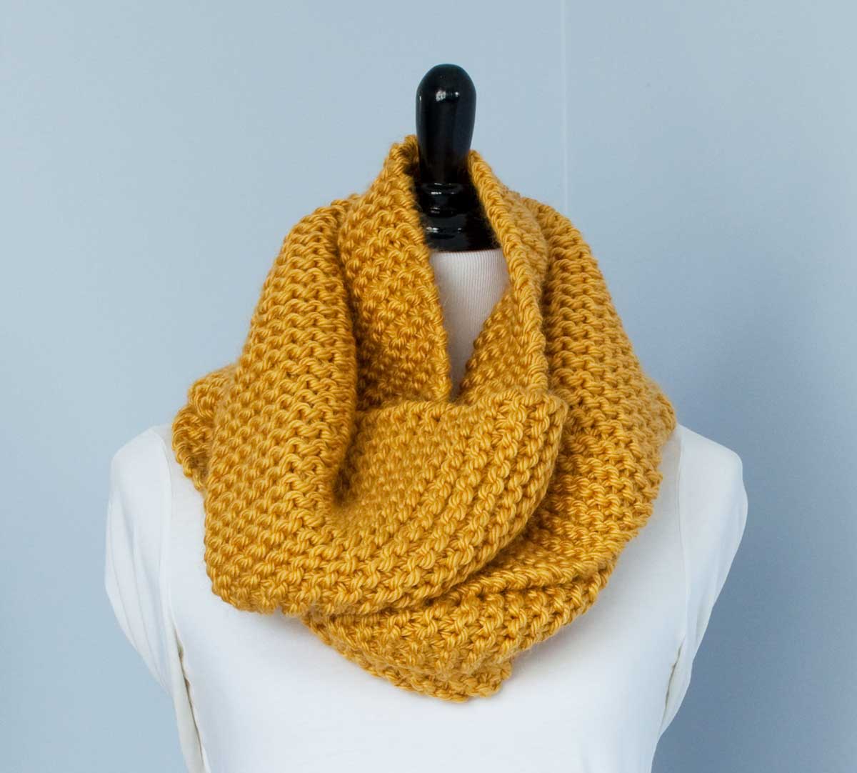 Close-up of mustard yellow scarf knit in garter stitch, wrapped around a a dress-makers dummy.